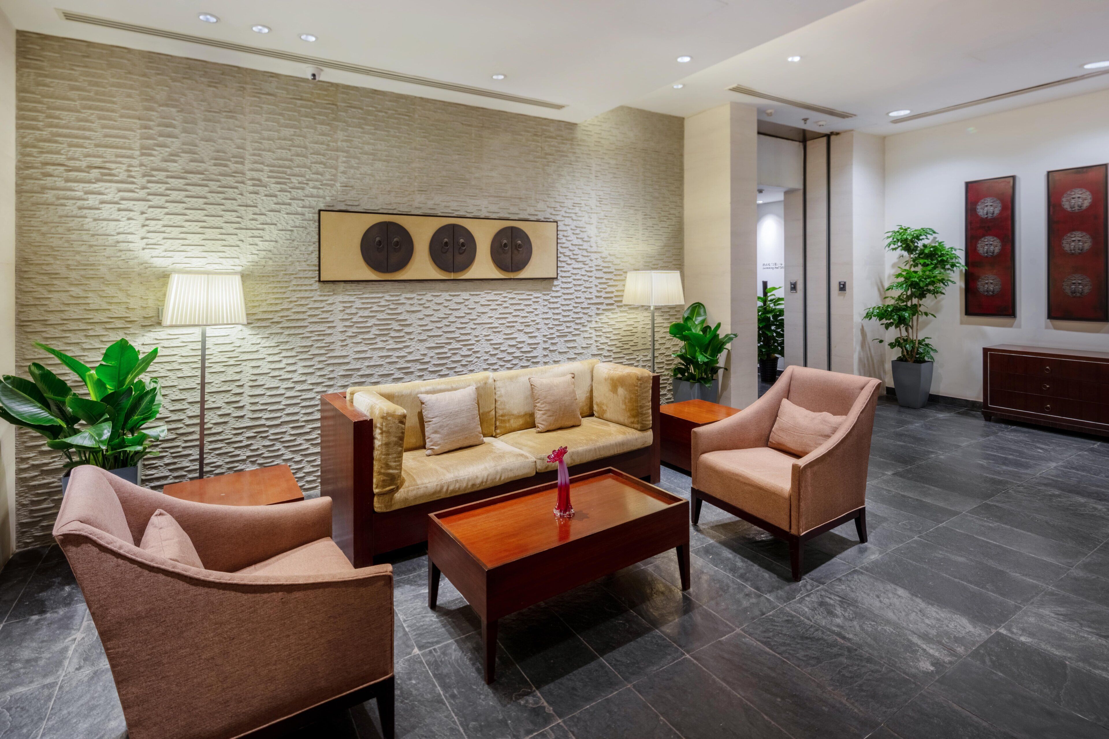 A modern lobby with a stone-textured wall, a sofa, two armchairs, a coffee table, and two floor lamps.