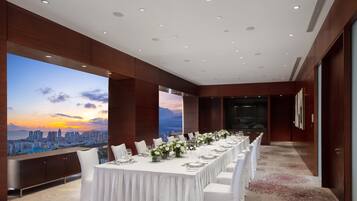 A long dining table set for a formal event with a cityscape view.
