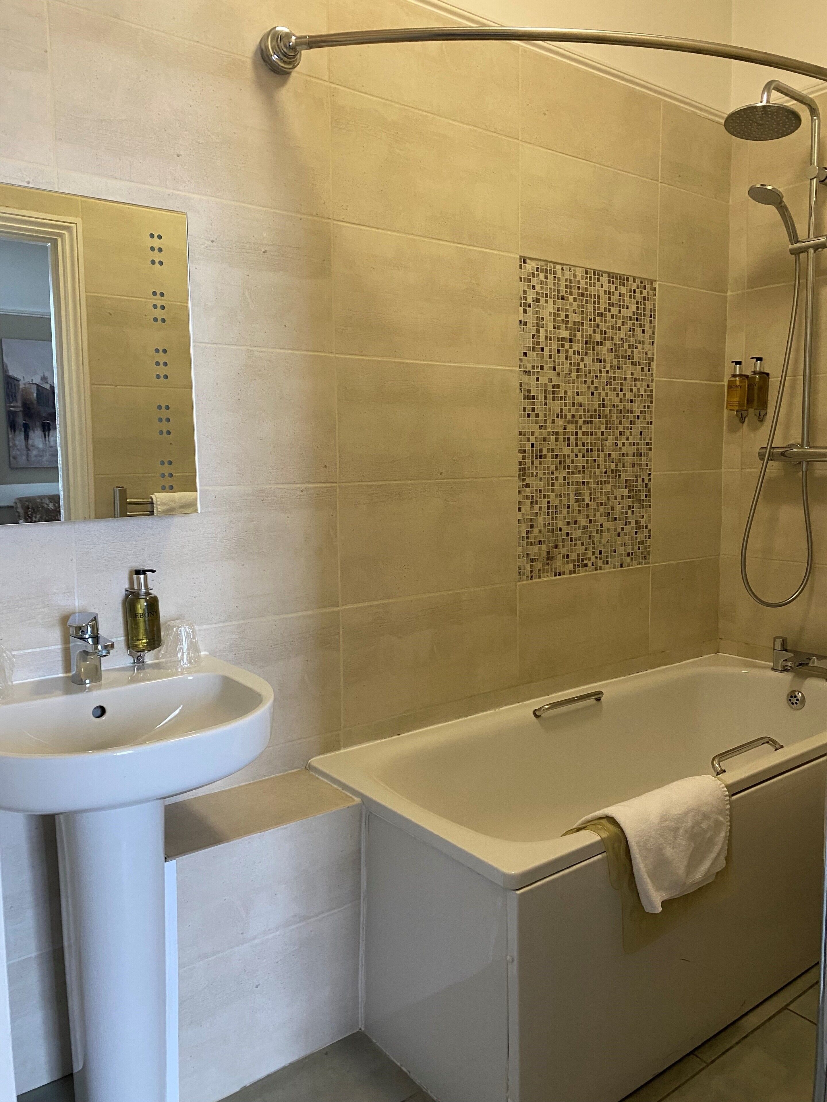 A bathroom with a sink, mirror, shower, and tiled walls.