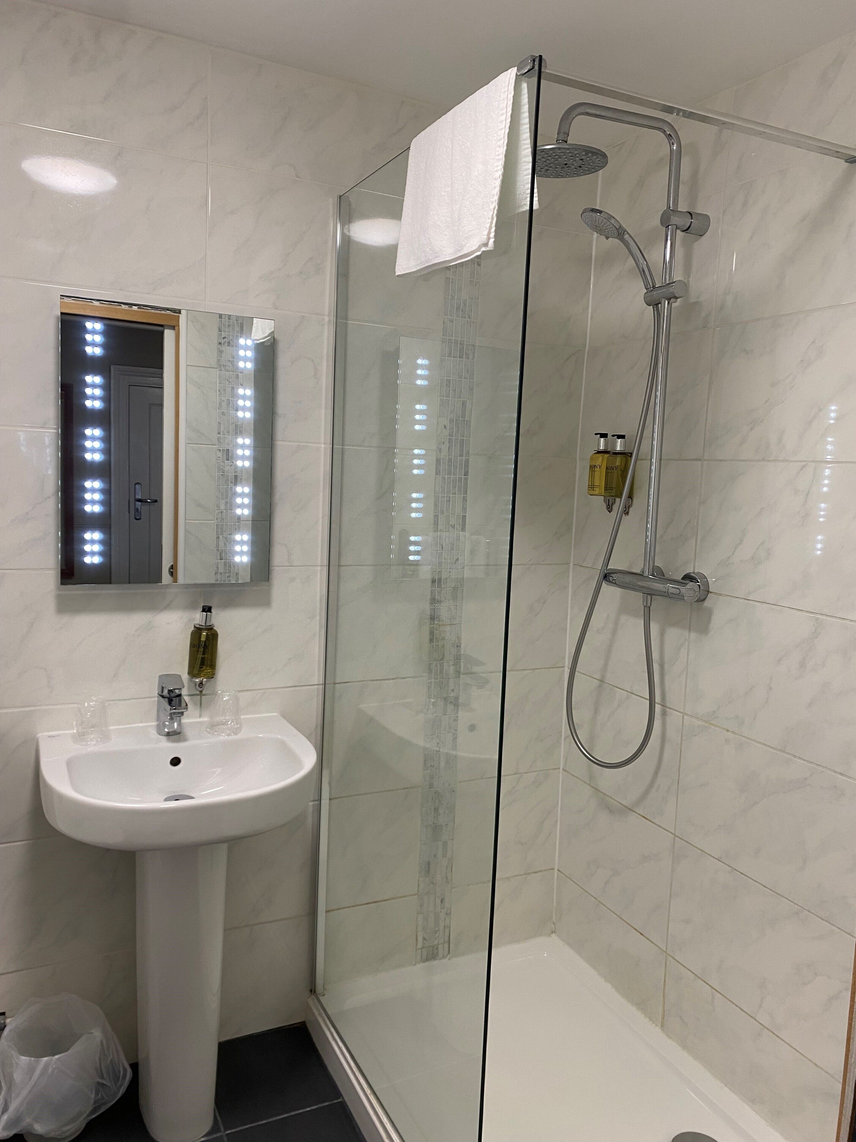 Ein modernes Badezimmer mit einer gläsernen Dusche, einem weißen Waschbecken und einem Spiegel mit LED-Beleuchtung.