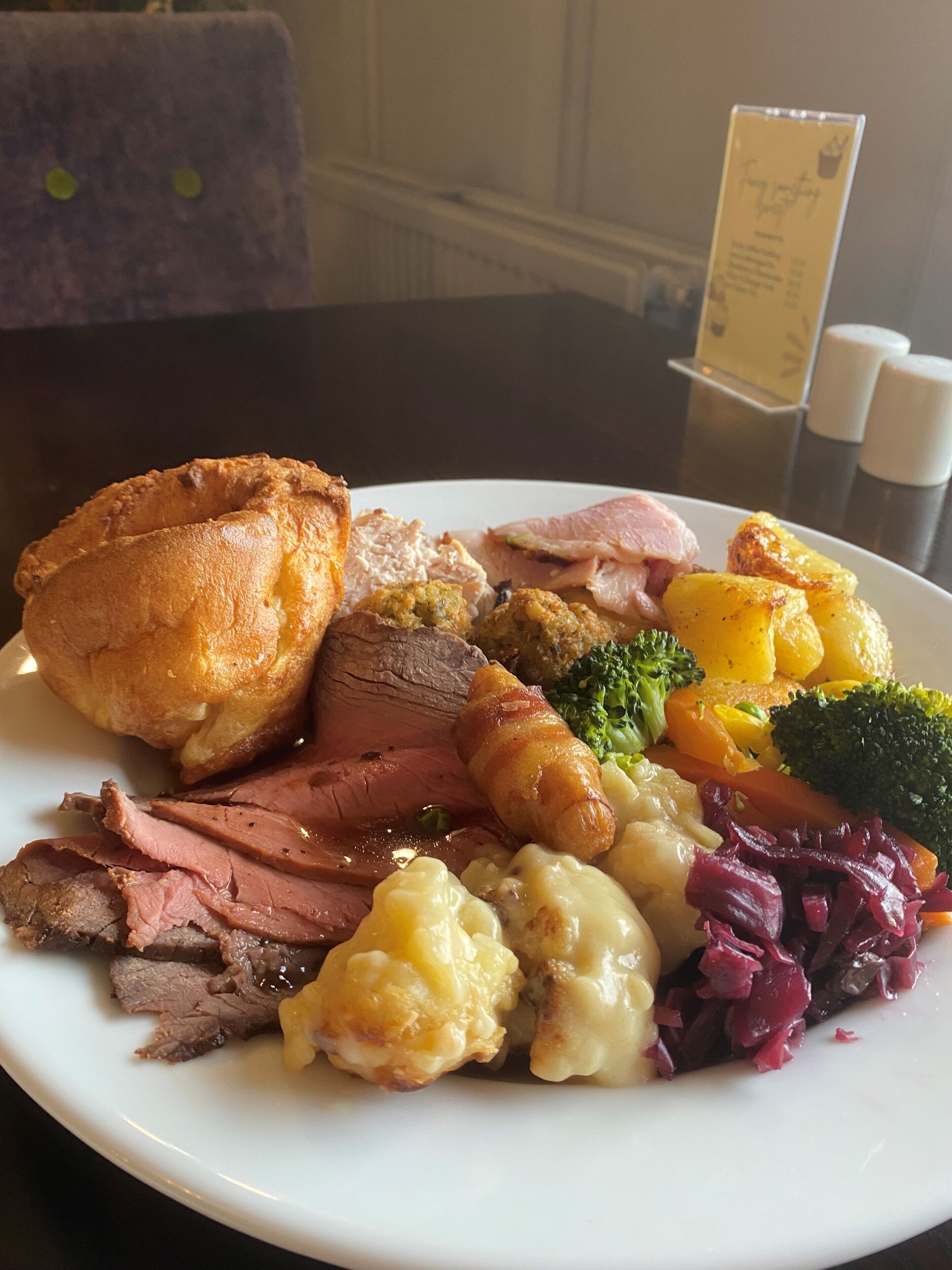 A plate of food including roast beef, Yorkshire pudding, potatoes, broccoli, and red cabbage.