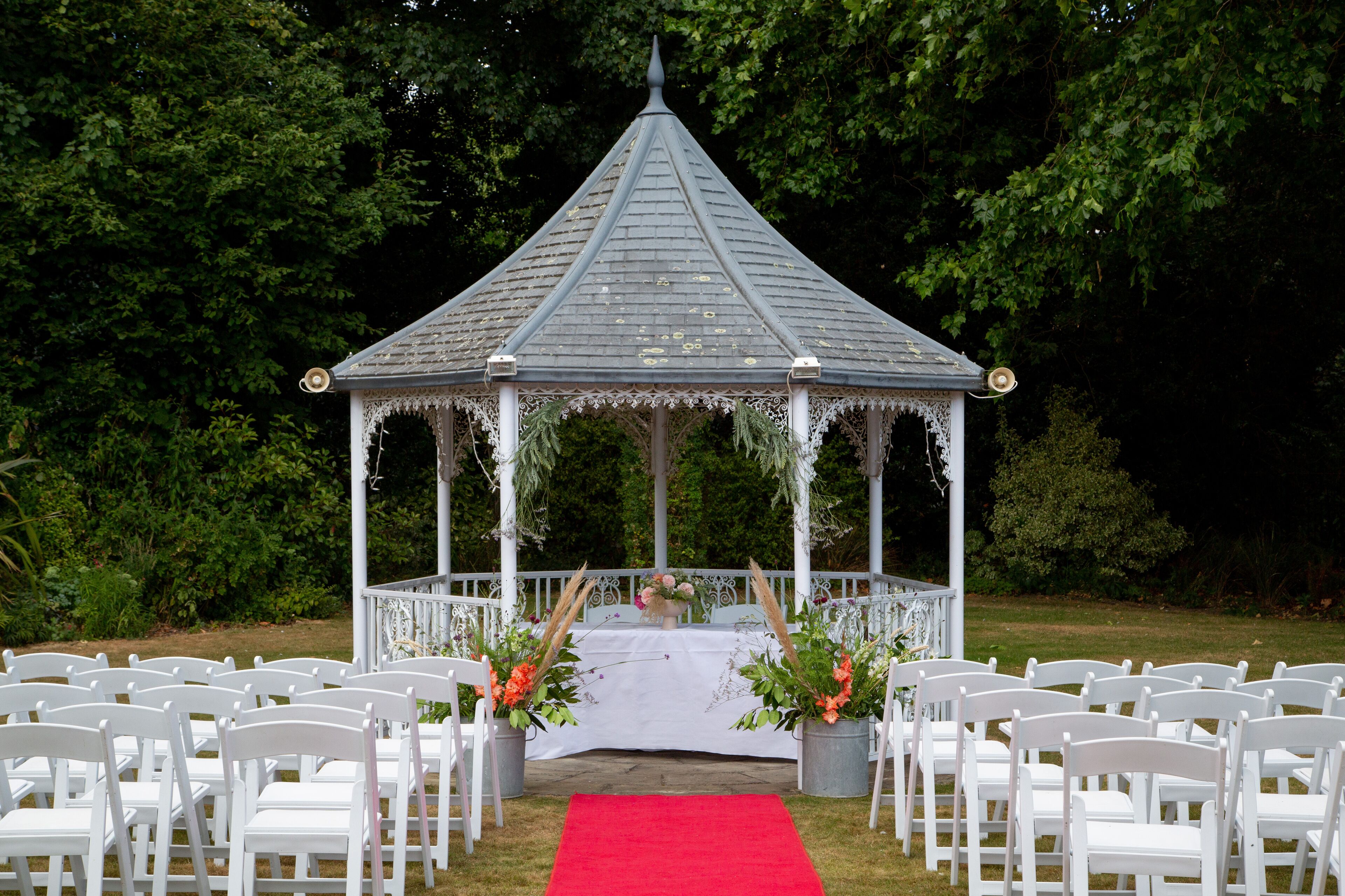 A gazebo with a white railing and a red carpet leading to it.