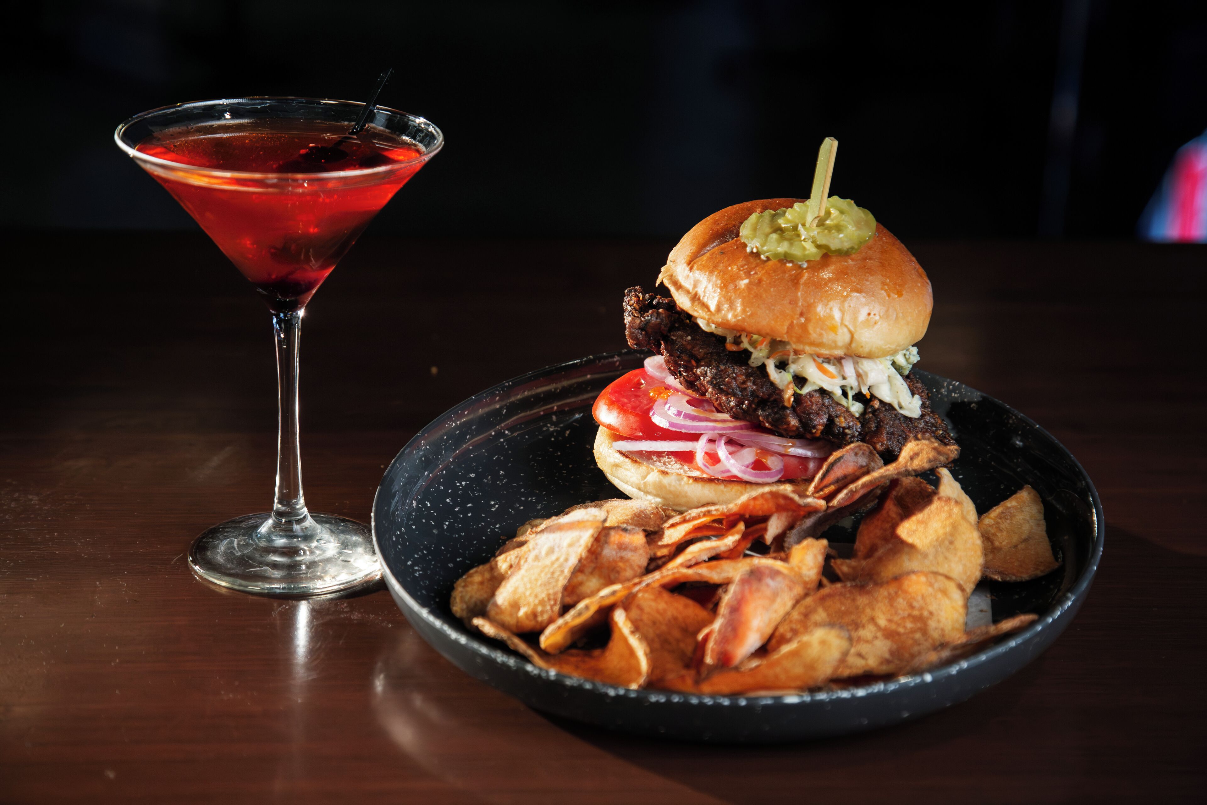 A martini glass and a plate with a burger and chips.