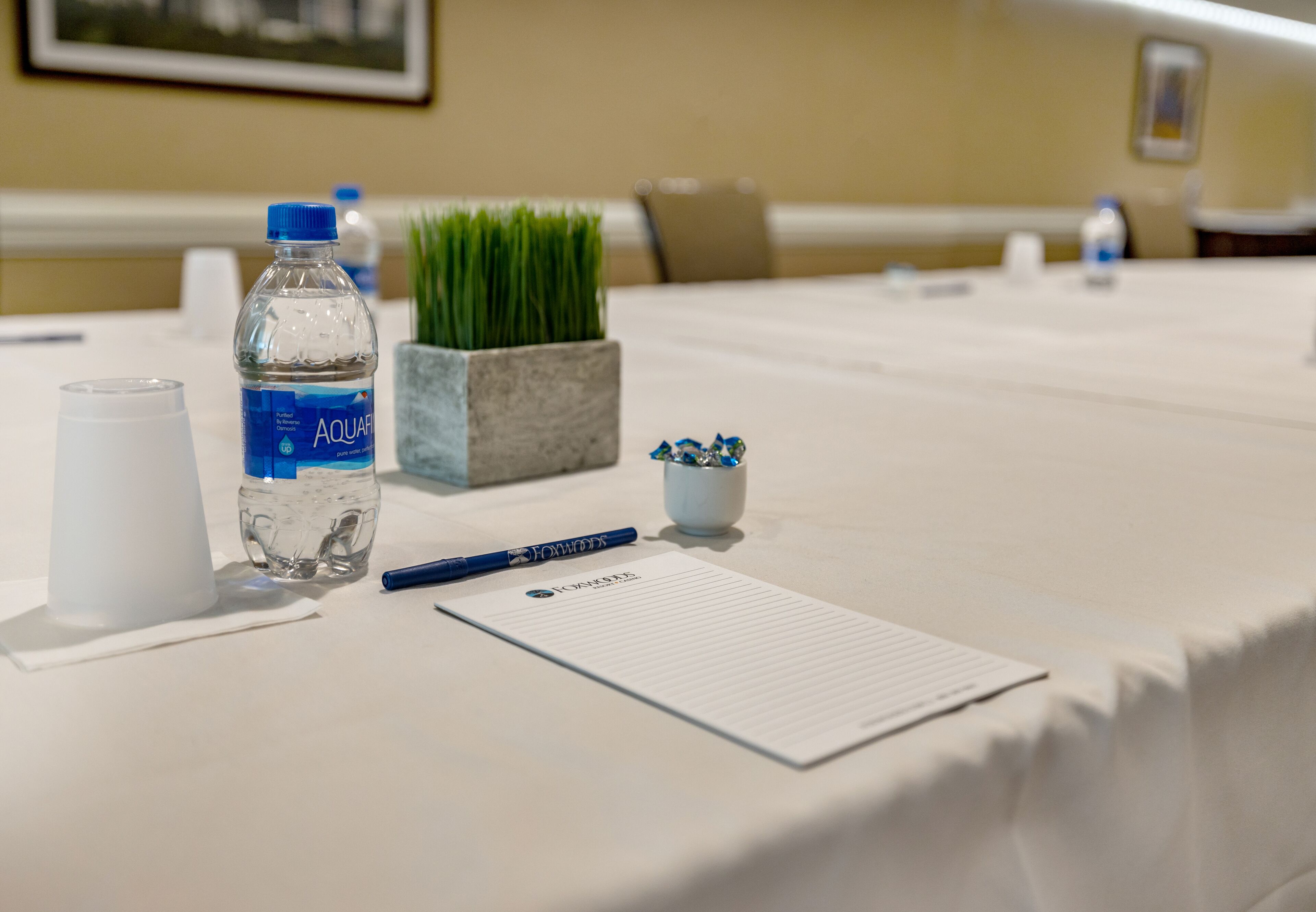 Una mesa de conferencias con una botella de agua, un bolígrafo, un bloc de notas y un pequeño estuche con bolígrafos.