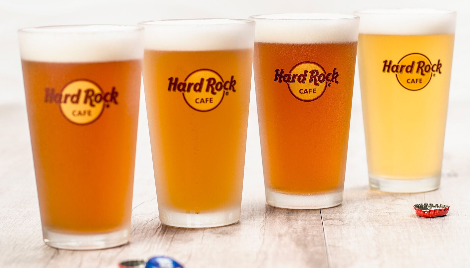 Four glasses of beer with the Hard Rock Cafe logo, placed on a wooden surface.
