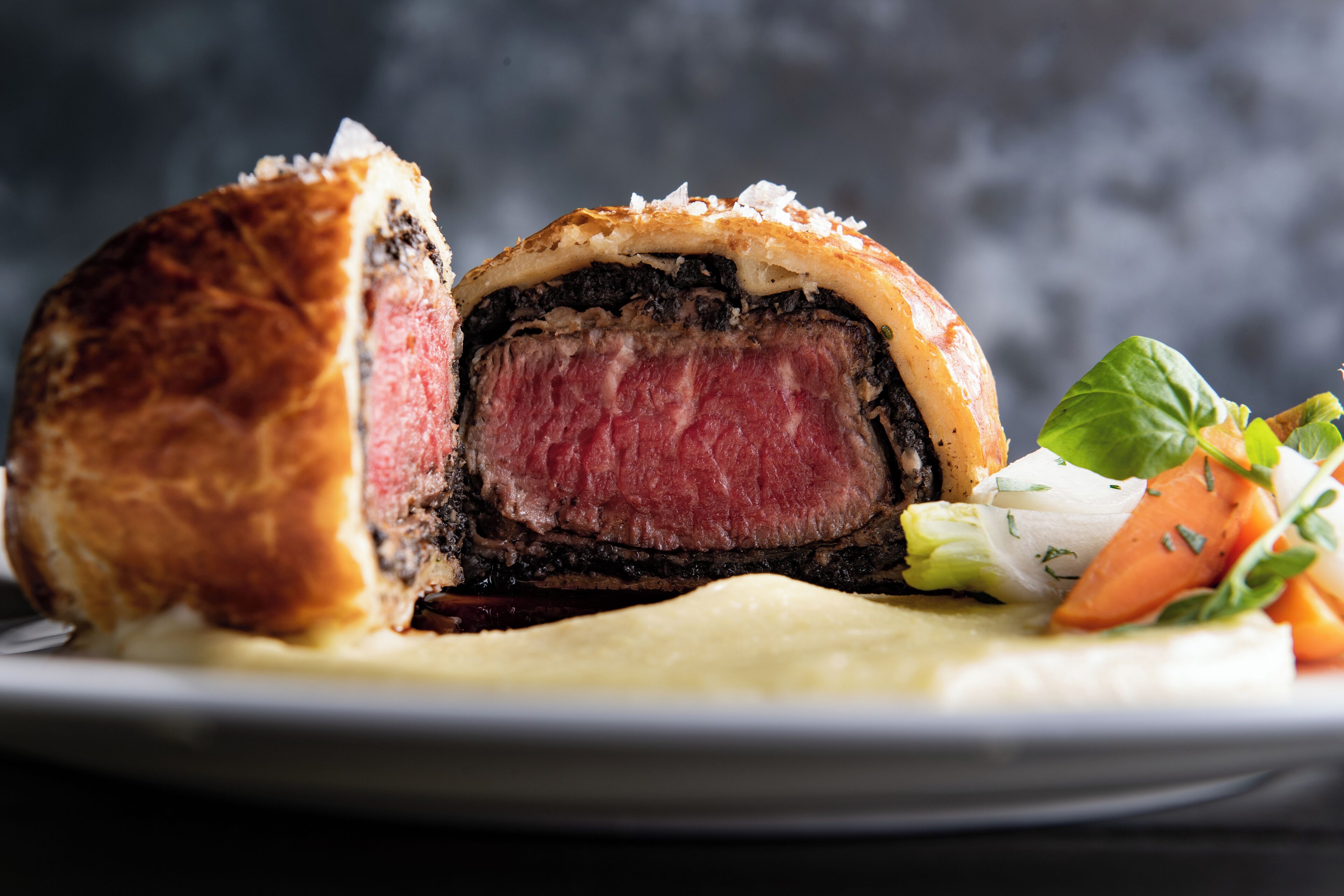 A steak with a crust, served with vegetables and a side of sauce.