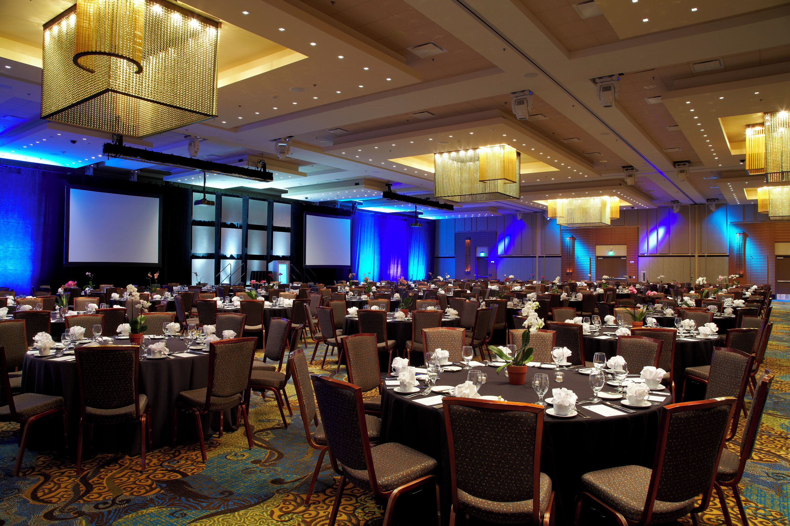A banquet hall with round tables set for dining, equipped with chairs, and decorated with flowers and table settings.
