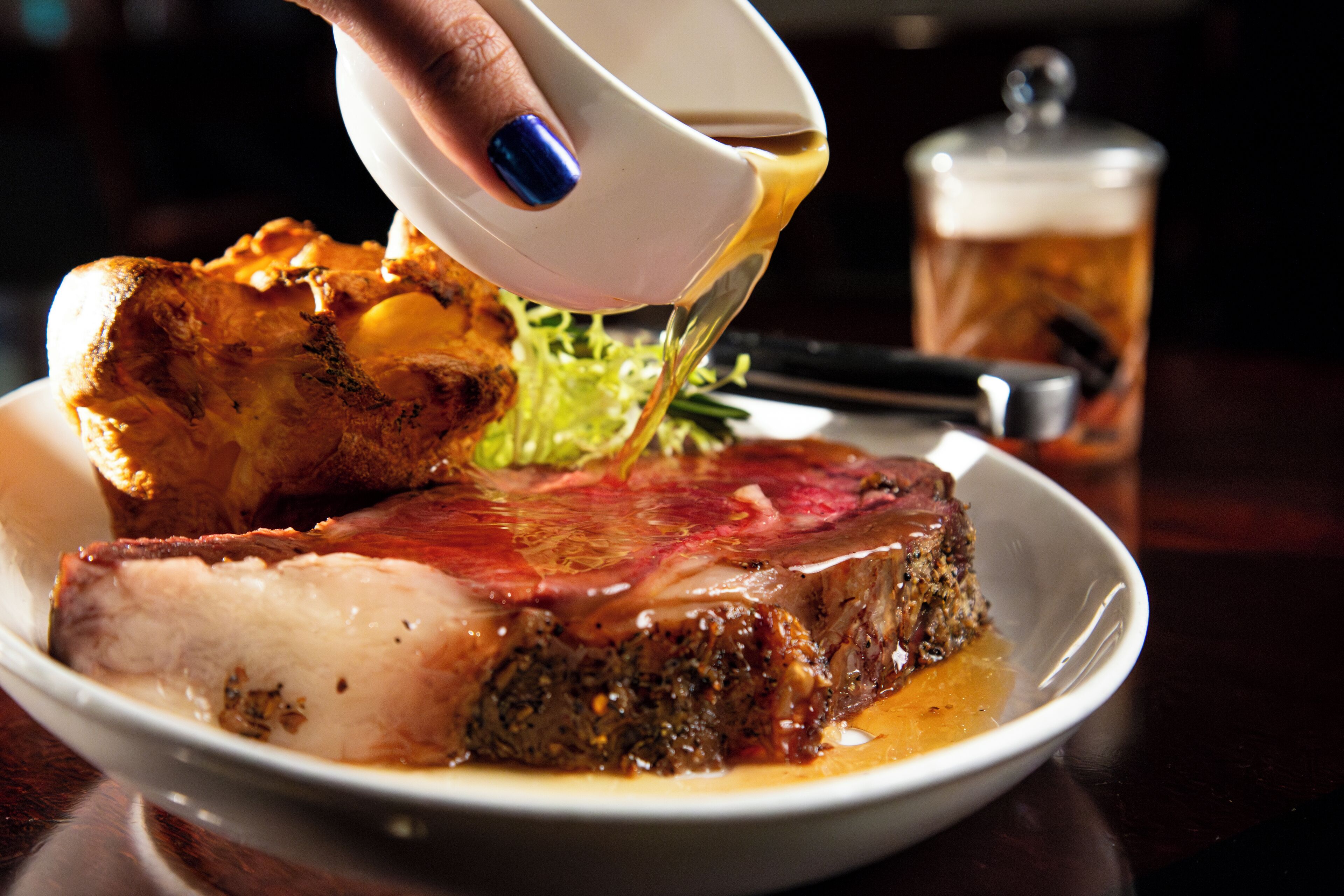 A plate of food with a large piece of meat and vegetables, and a hand pouring sauce over it.