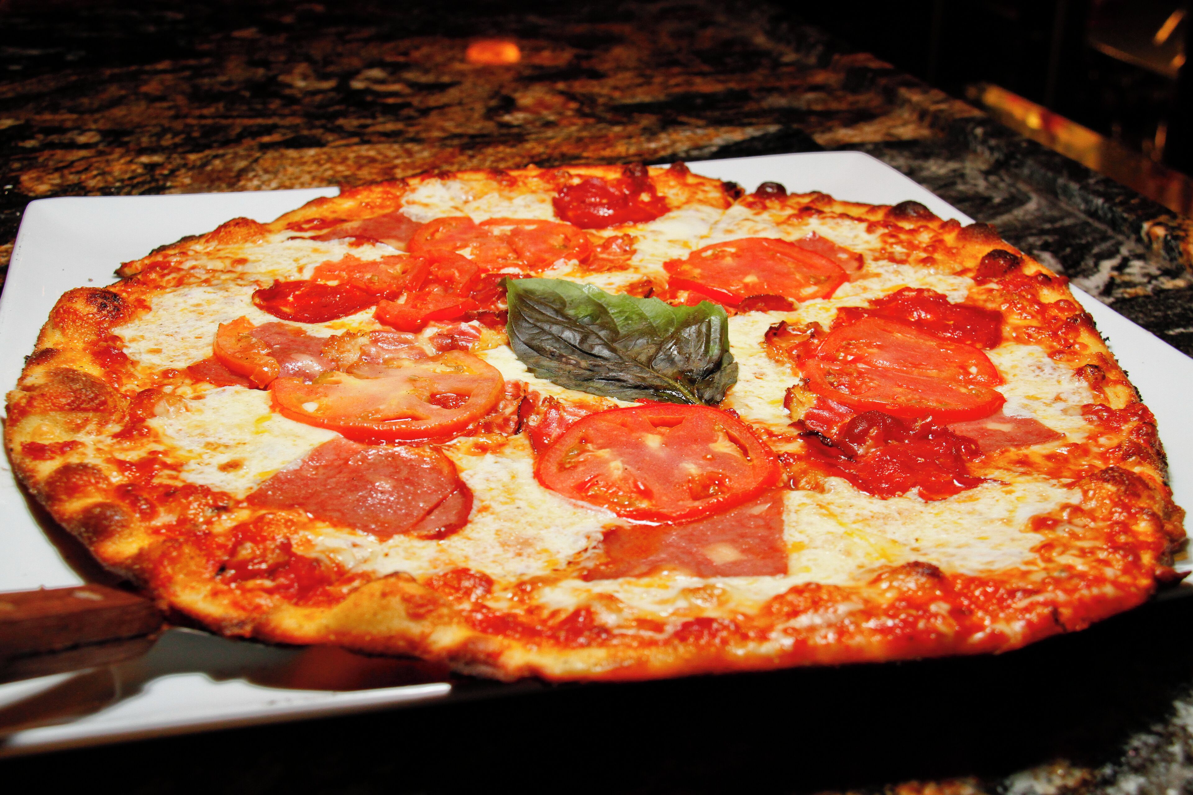 Pizza com rodelas de tomate e manjericão sobre um prato branco.