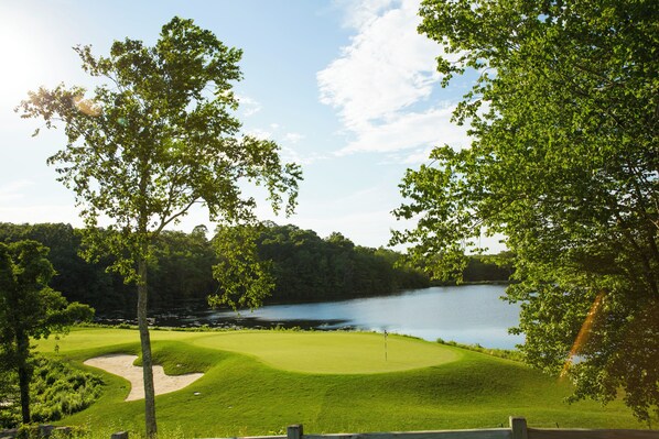 A golf course with a water body in the background and lush greenery. - Great Cedar Hotel at Foxwoods (Mashantucket)