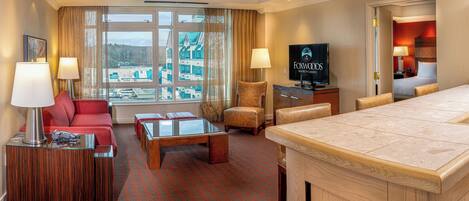 A hotel room with a large window, a TV, a sofa, a coffee table, and a dining area.