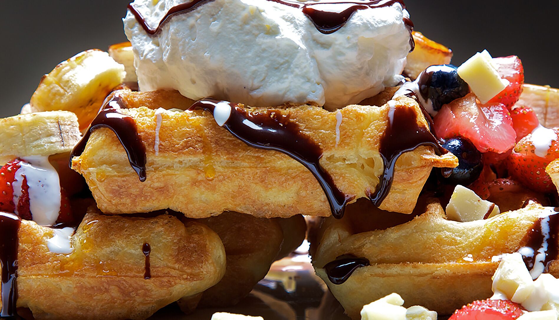 A stack of pancakes with chocolate syrup and whipped cream.