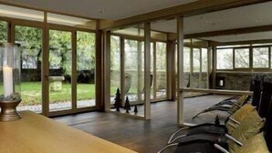 A modern interior with large glass doors leading to a garden, a wooden table, and a row of chairs. - Hotel Schloss Waldeck (Waldeck)