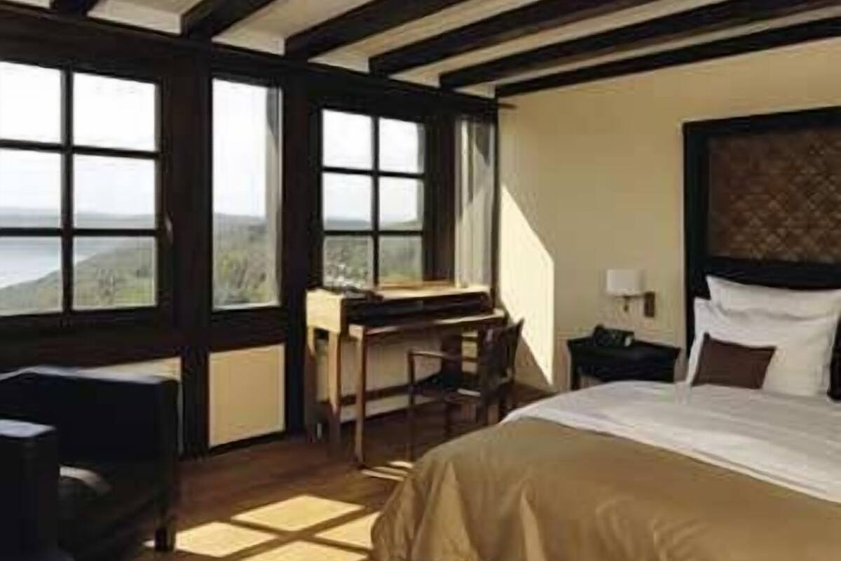 A bedroom with a bed, a desk, and a chair. There is a window with a view of the outdoors.