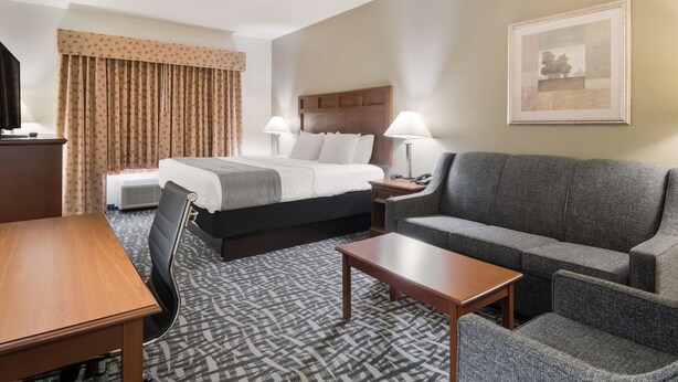 A hotel room with a bed, a sofa, a desk, and a patterned carpet. - Best Western Comanche Inn (Comanche)