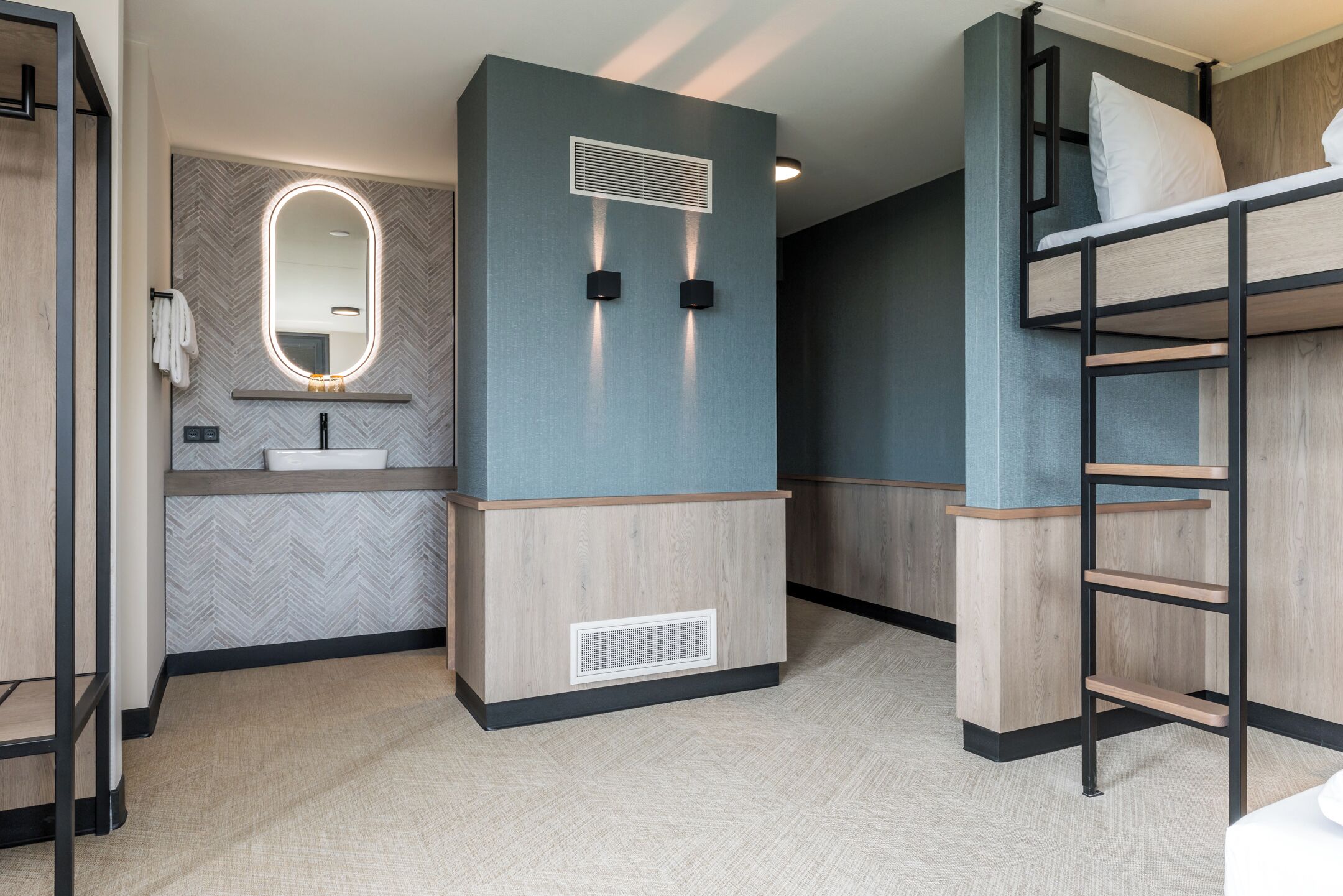 Una cama litera con escalera, un espejo con luces, un lavabo y un sistema de ventilación.