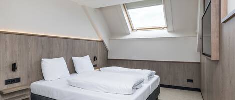 Un dormitorio moderno con tragaluces, una cama con ropa de cama blanca, cabecera de madera y estante empotrado para televisor.