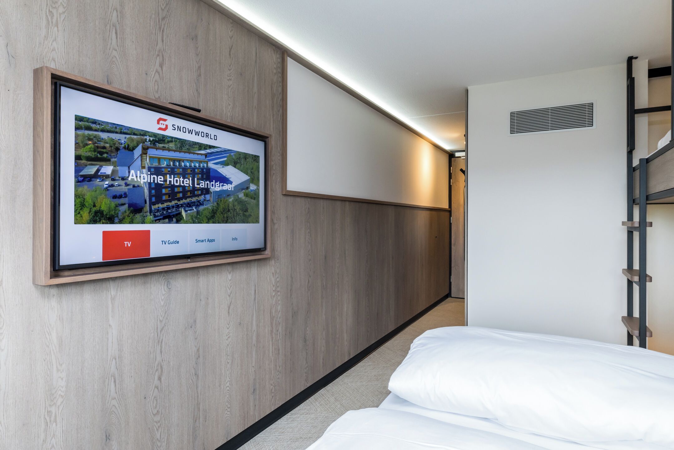 Habitación de hotel con un televisor de pared que muestra una imagen del hotel, una cama y una pared de madera.