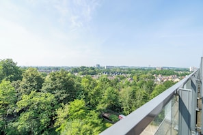 Un immeuble de grande hauteur offrant une vue sur une zone densément boisée et sur des bâtiments situés au loin.