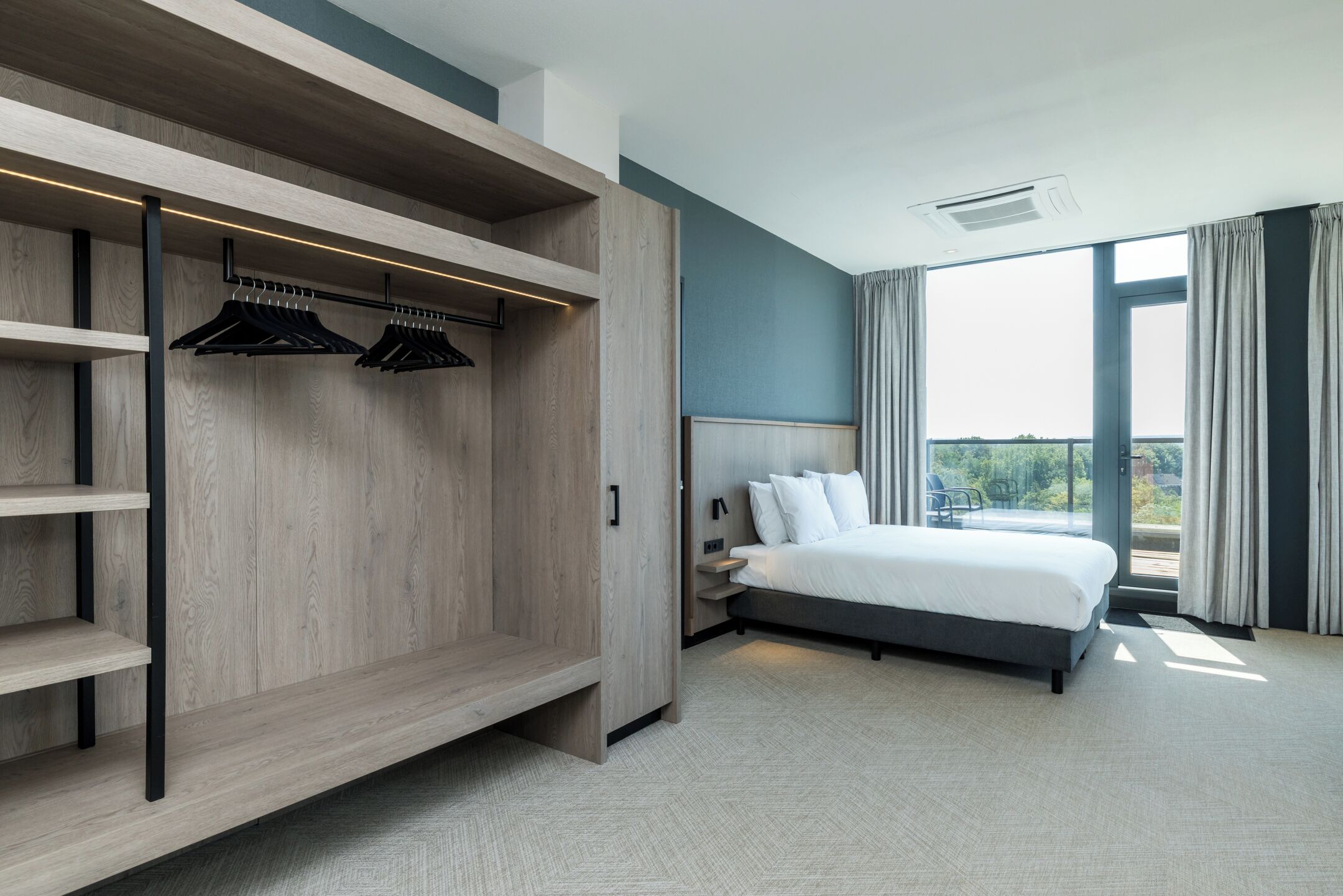 Habitación de hotel moderna con una cama grande, un vestidor con estantes de madera y un balcón con vistas.