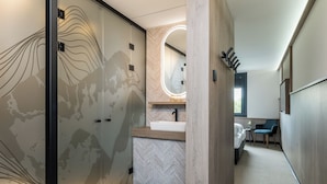 A modern bathroom with a herringbone patterned wall, a round mirror with a light, a sink, and a chair.