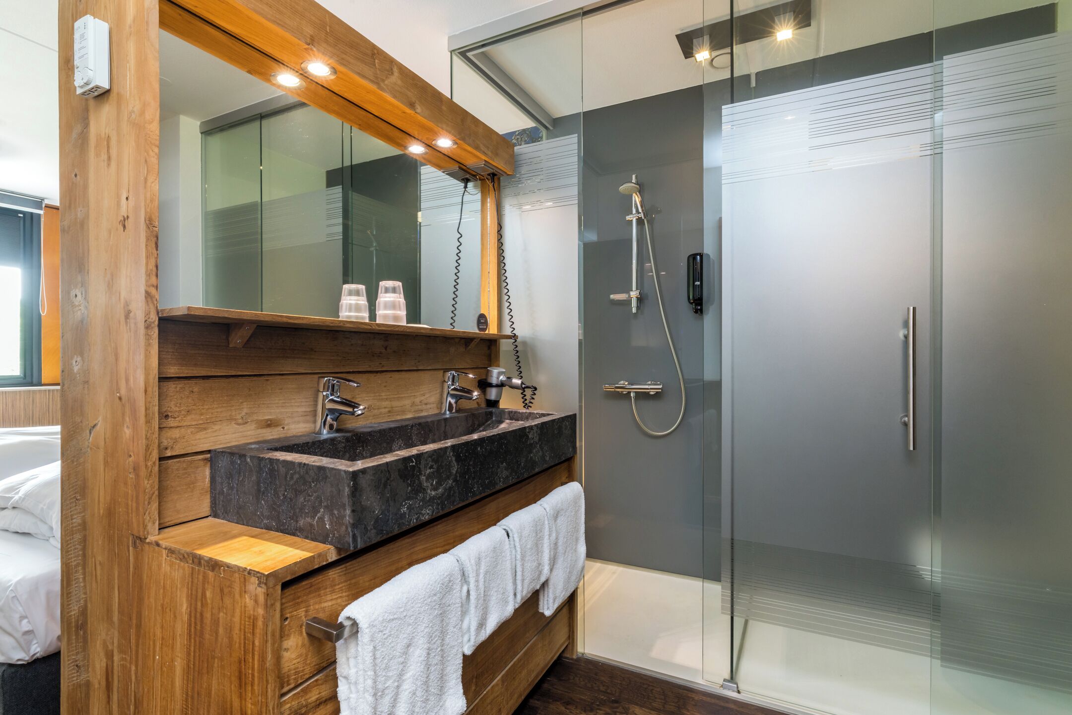 Une salle de bain avec un meuble-lavabo en bois, deux vasques, un miroir et une douche à parois de verre.