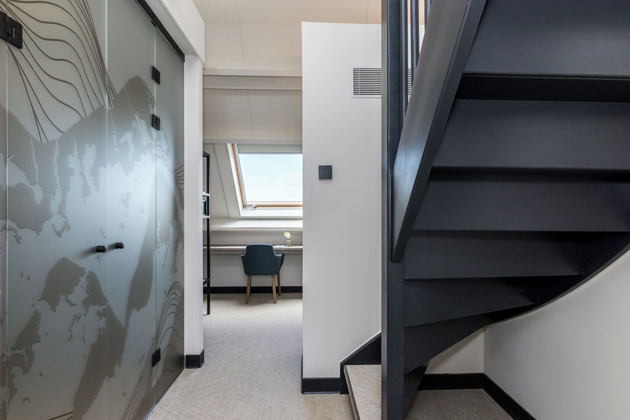 Ein modernes Interieur mit einer Treppe, einem Schreibtisch mit Stuhl und einem Fenster mit Tageslicht.