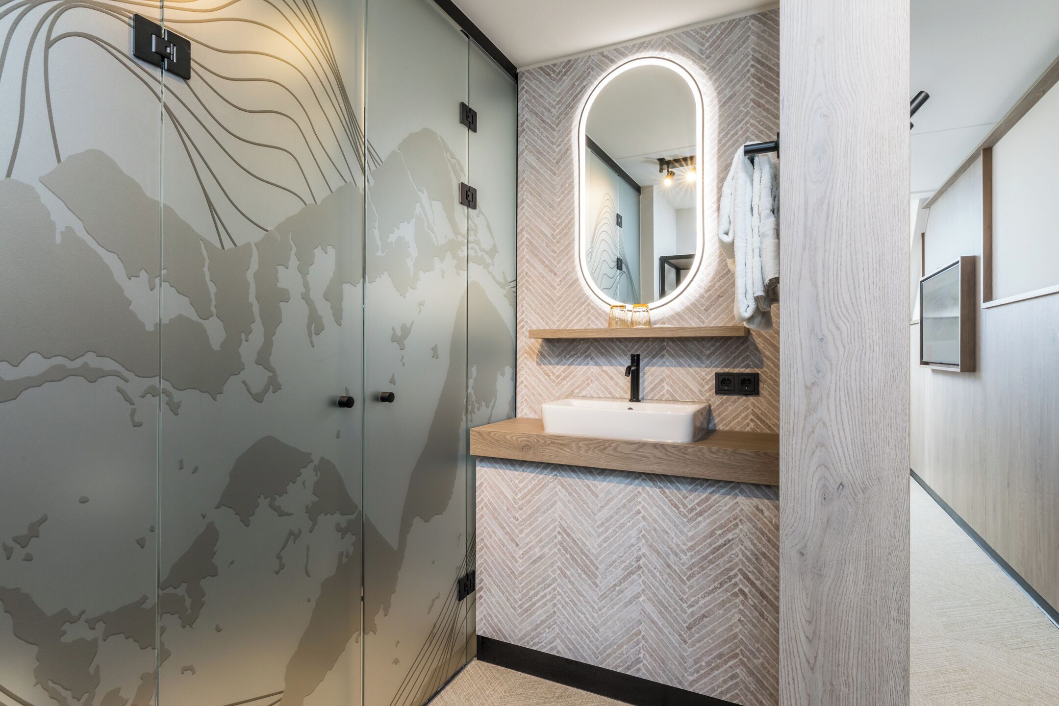 Un baño con pared de diseño chevron, un lavamanos blanco, un espejo con marco ovalado y un perchero para toallas.