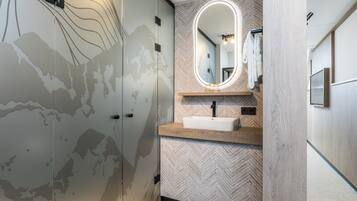 Un baño con pared de diseño chevron, un lavamanos blanco, un espejo con marco ovalado y un perchero para toallas.