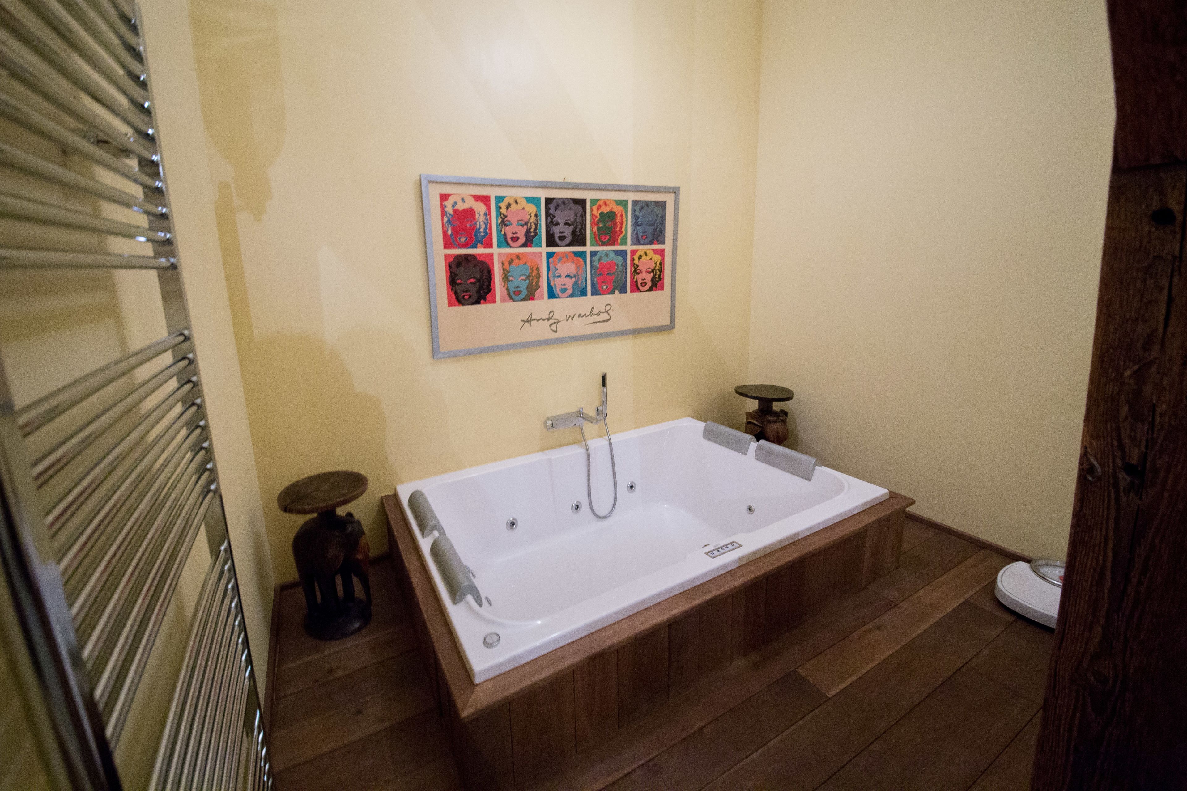 Un baño con una bañera grande, piso de madera, un perchero y una obra de arte enmarcada en la pared.