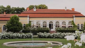 A building with a red-tiled roof, arched windows, and a fountain in the garden.