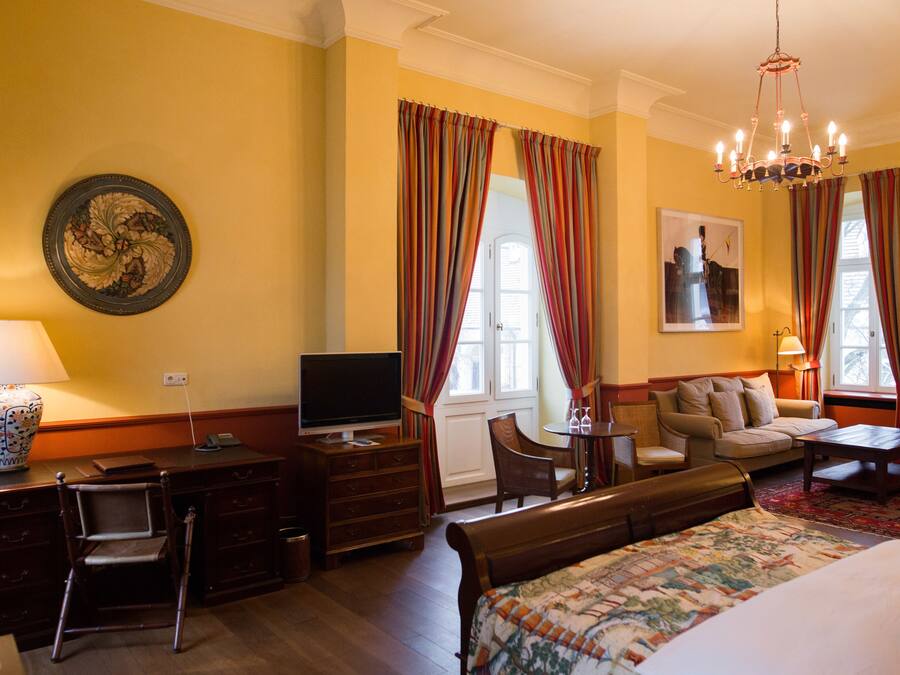Une chambre d’hôtel comprenant un lit, un bureau avec une télévision, une chaise, un canapé et un lustre.