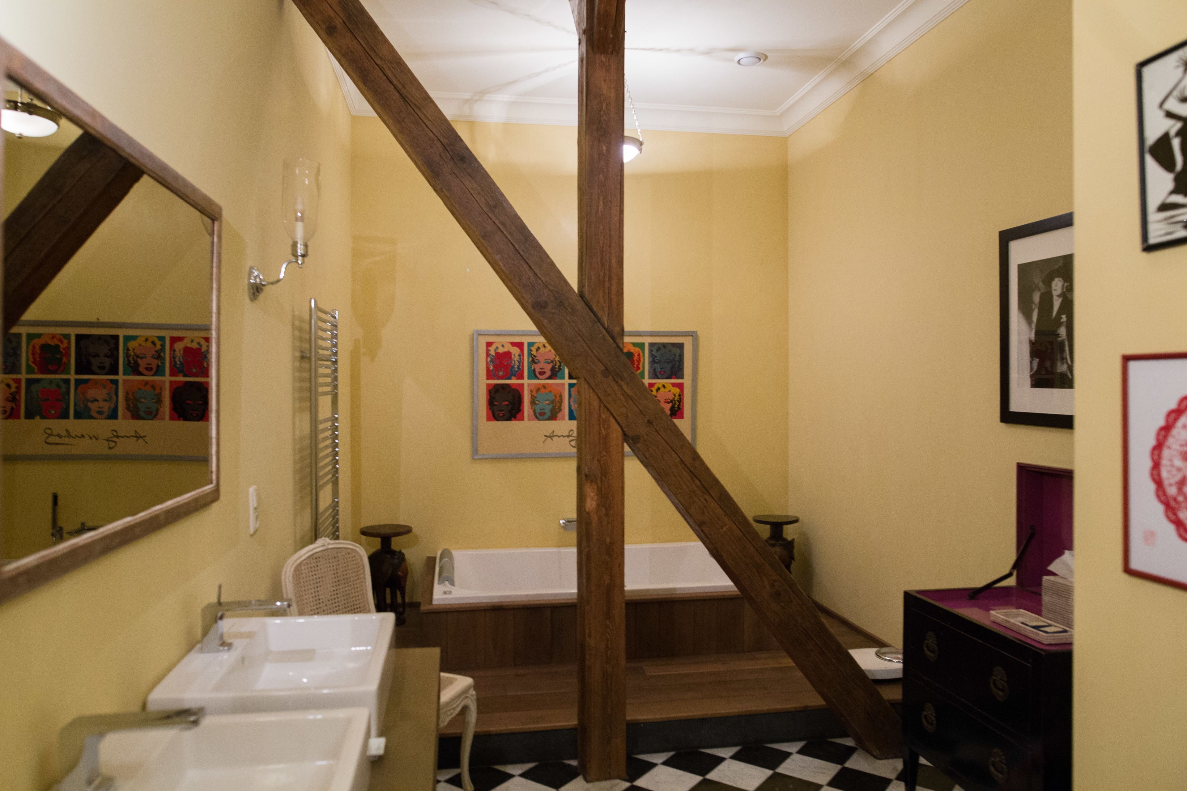 A bathroom with a wooden staircase, two sinks, a bathtub, and framed artwork on the walls.