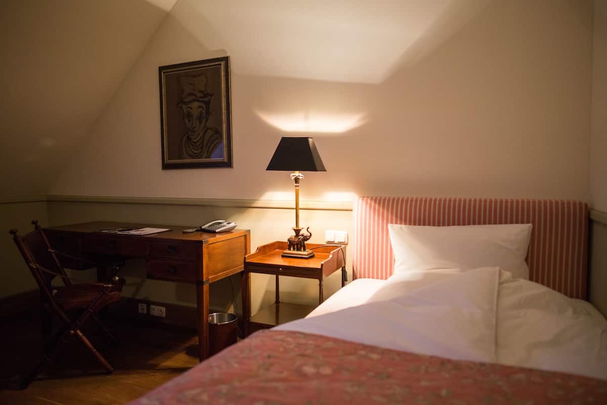 A hotel room with a bed, a desk with a telephone, a lamp, and a chair.