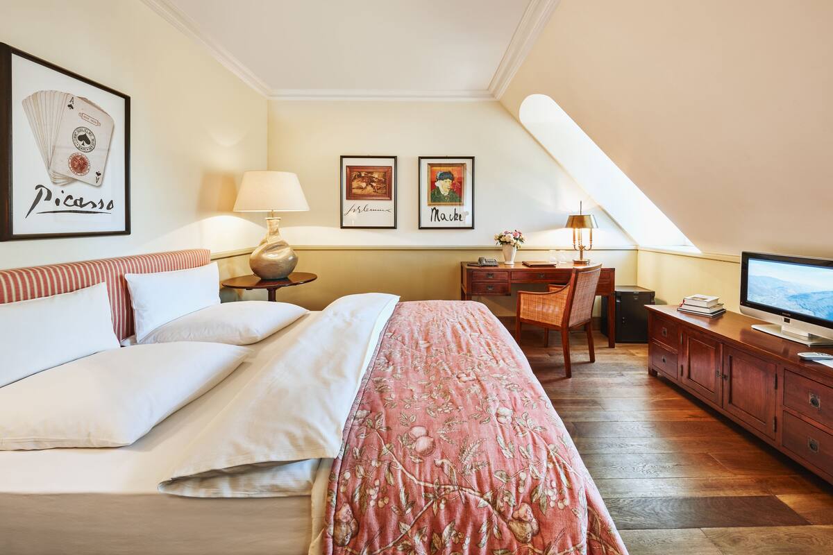 A hotel room with a bed, a desk with a computer, a TV, and artwork on the walls.