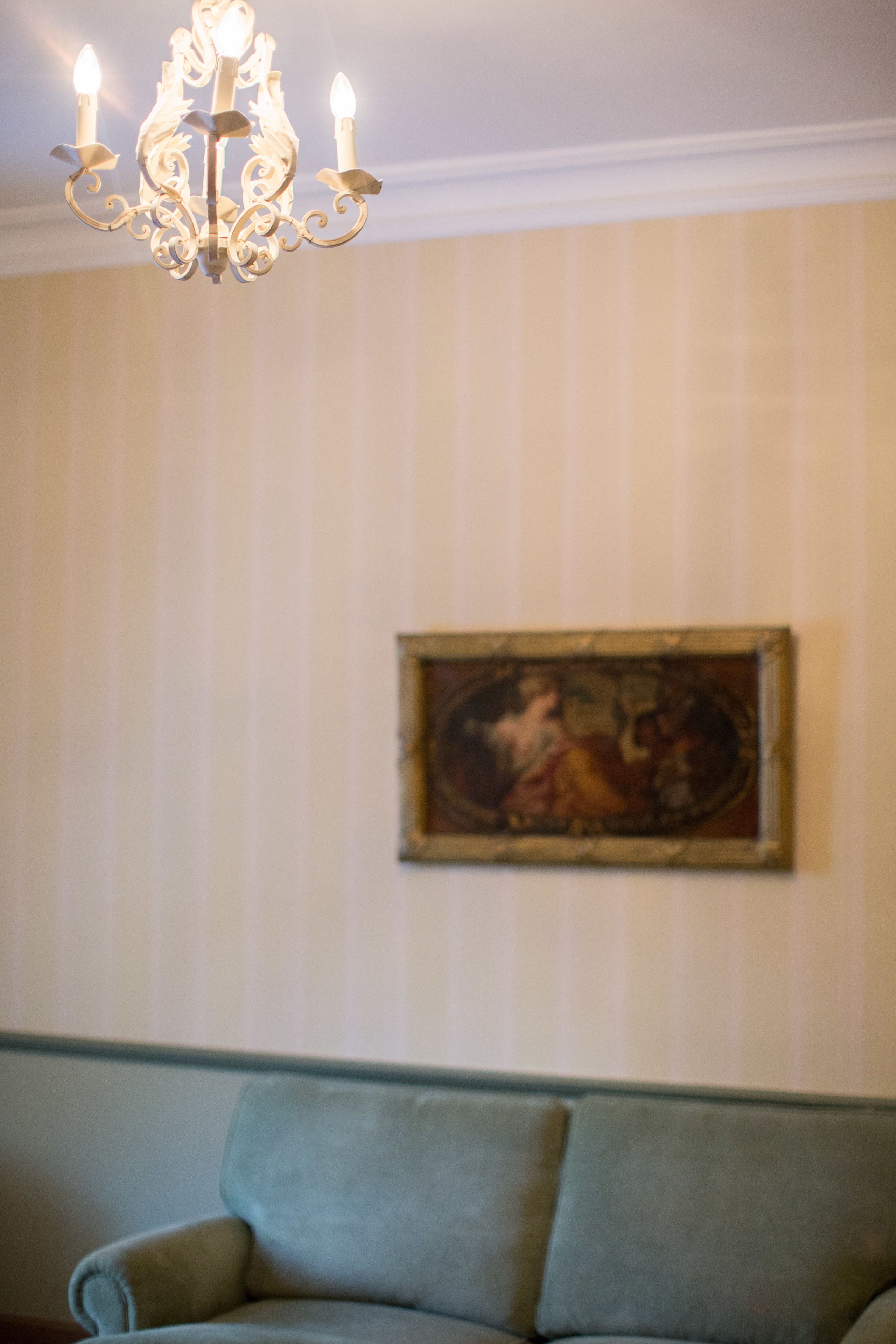 Una habitación con candelabro, un cuadro en la pared y un sofá verde.