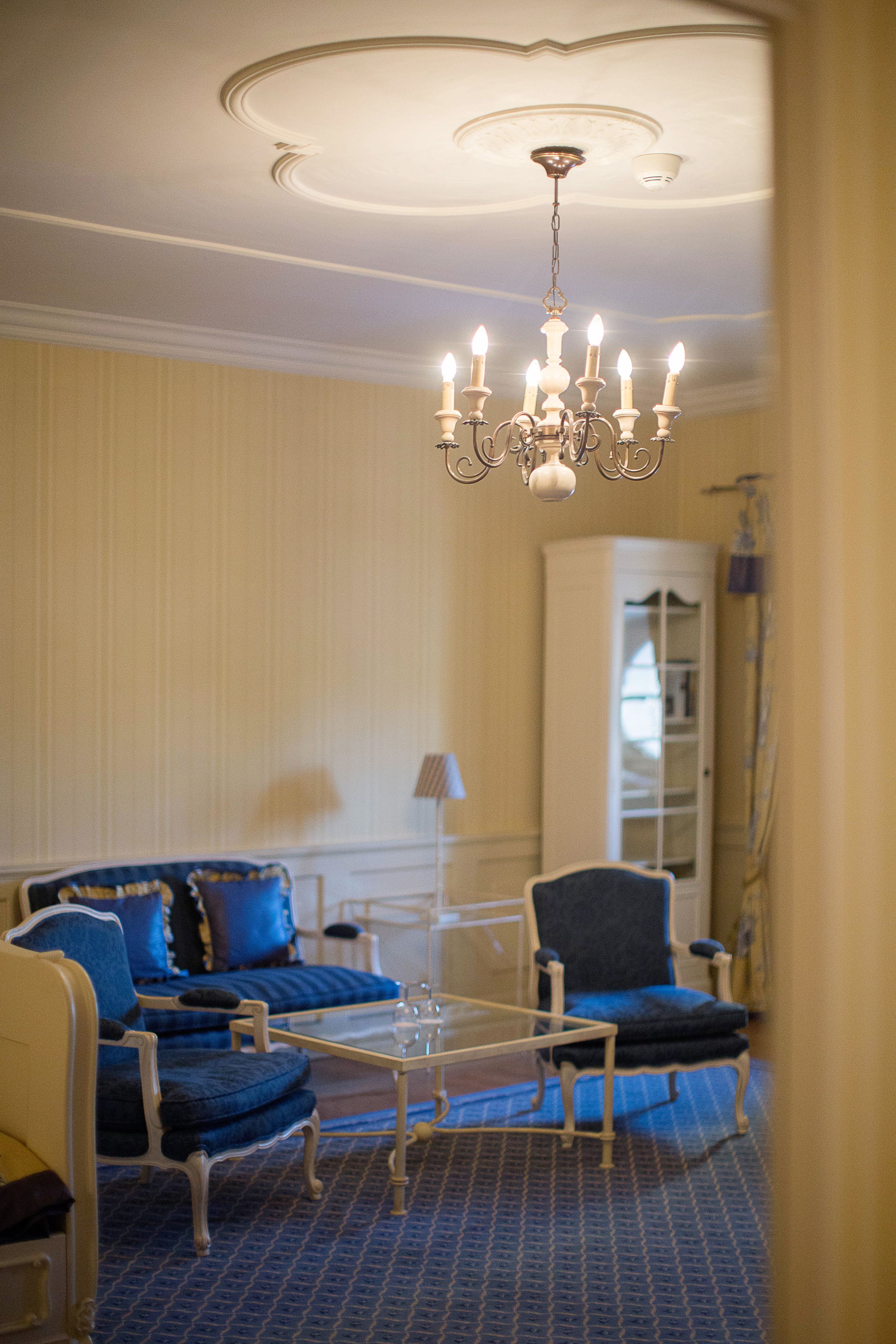 A room with a chandelier, a sofa set, a chair, and a cabinet.