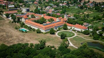 An aerial view of a large estate with multiple buildings, a circular driveway, and surrounding greenery.
