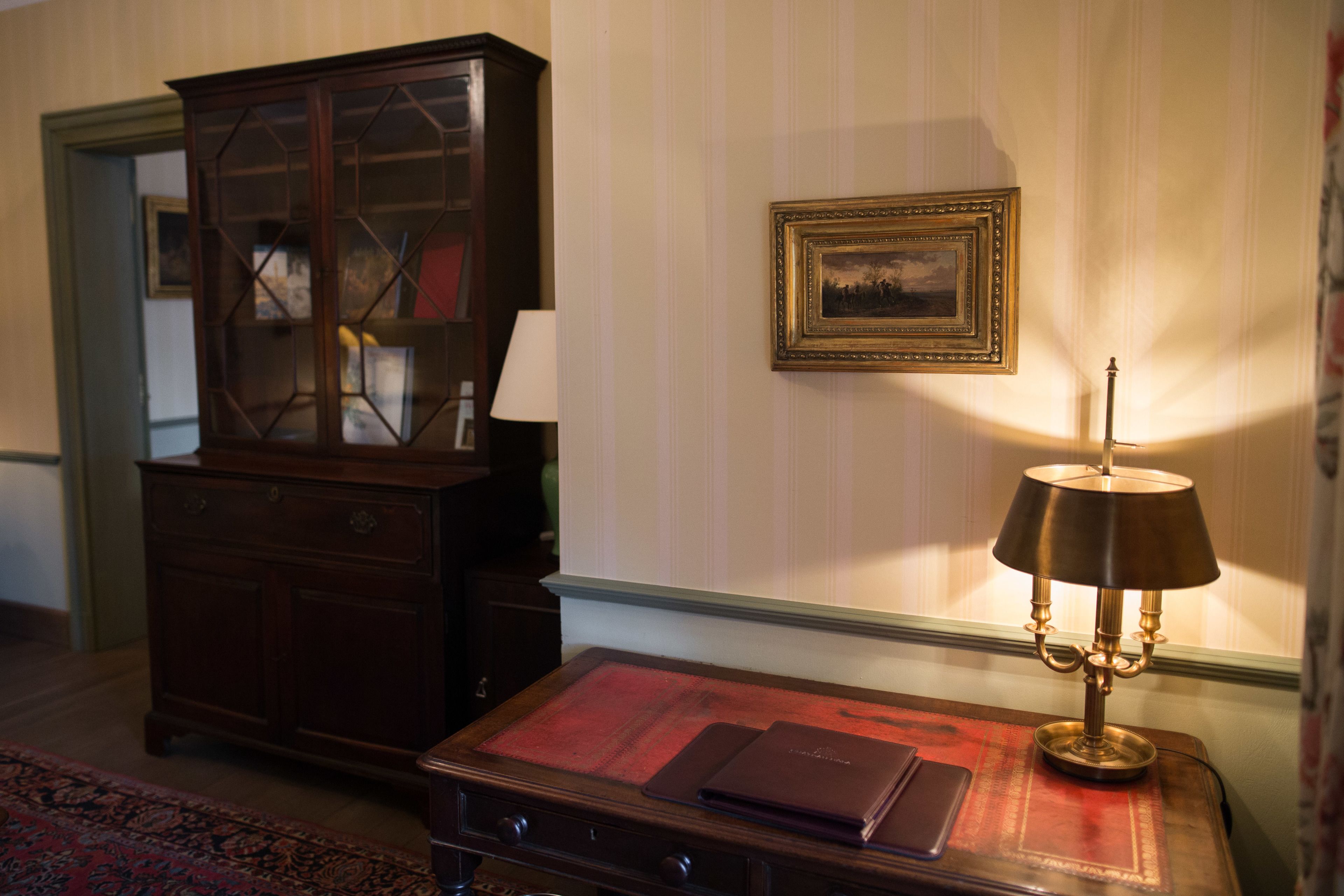 Una habitación con un armario de madera, una mesa con un tapete rojo, una lámpara y un cuadro en la pared.