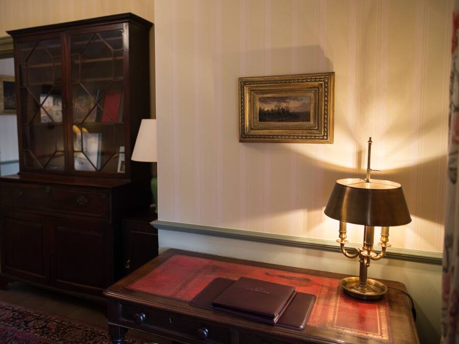 Una habitación con un armario de madera, una mesa con un tapete rojo, una lámpara y un cuadro en la pared.
