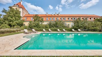 A swimming pool with lounge chairs, a large building with a red roof, and a clear blue sky.