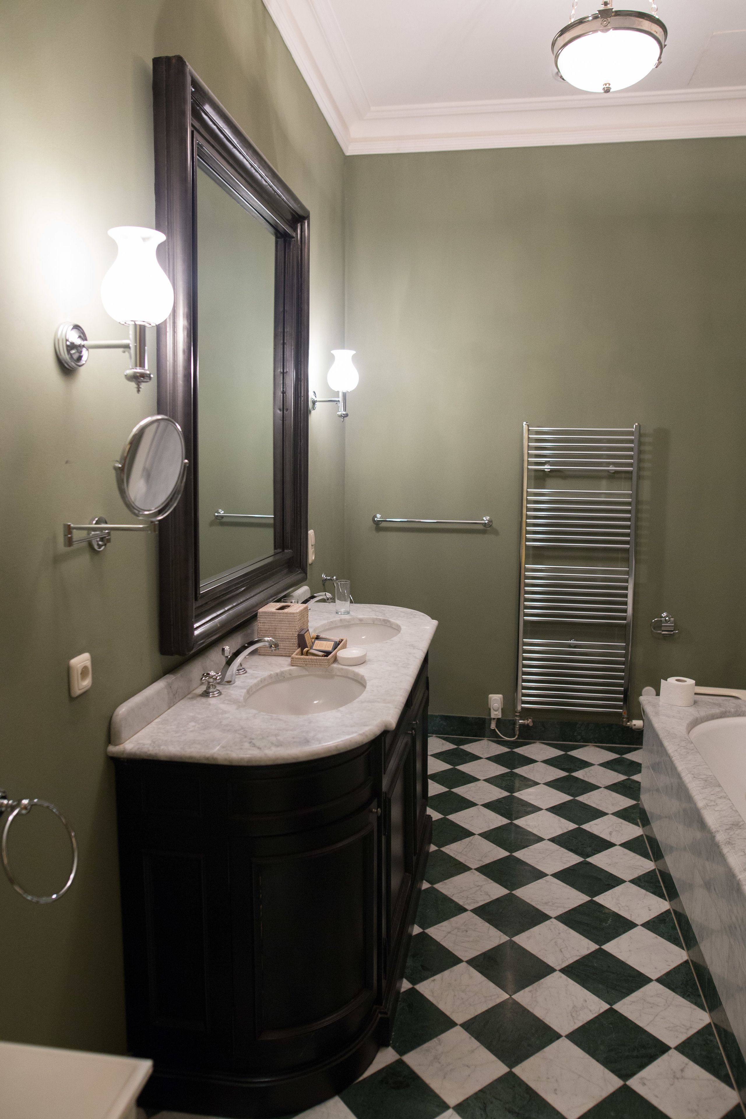 A bathroom with a double sink vanity, a large mirror, wall sconces, a towel rack, and a checkered floor.