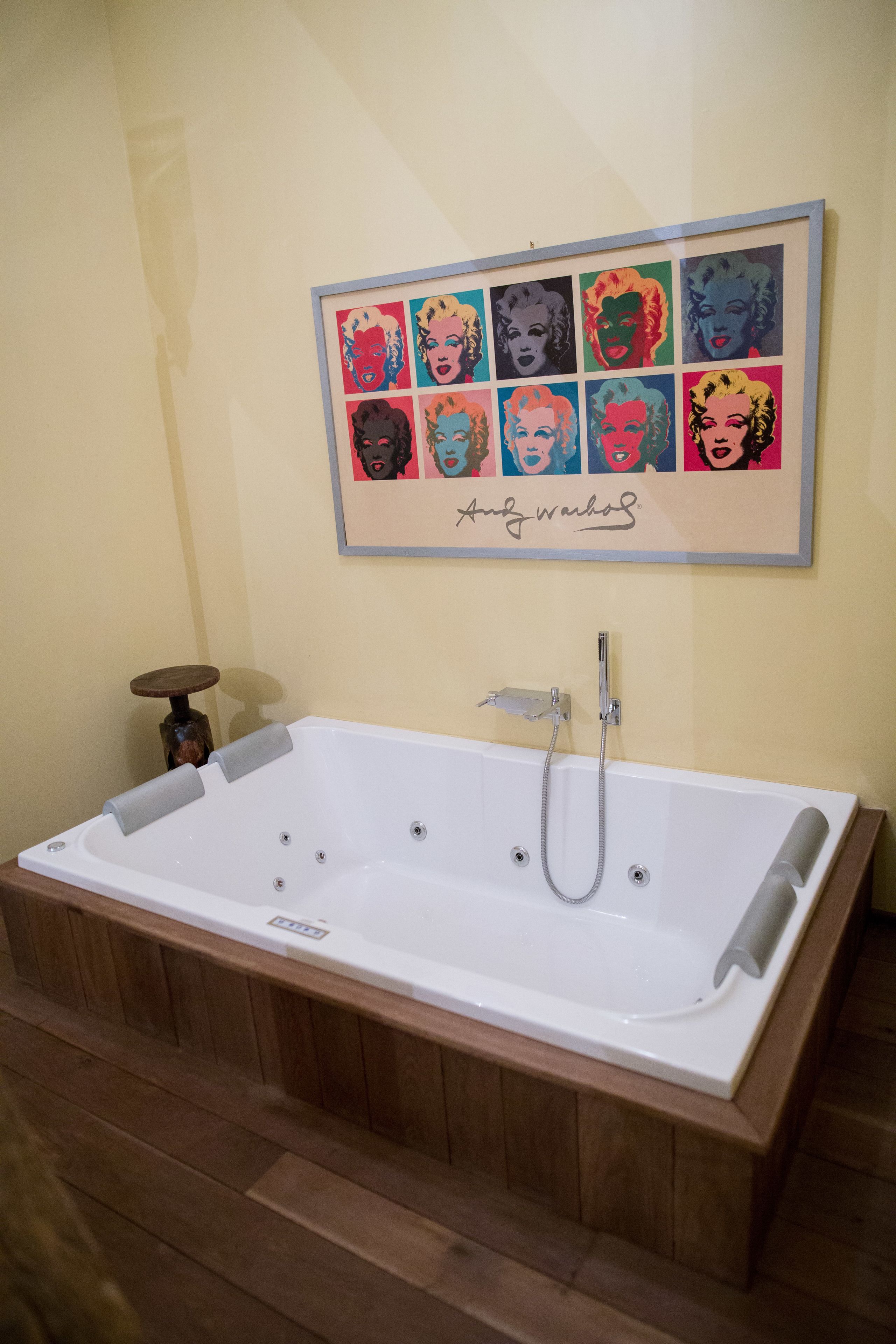 Un baño con una bañera grande, un cuadro pop art enmarcado en la pared y suelo de madera.