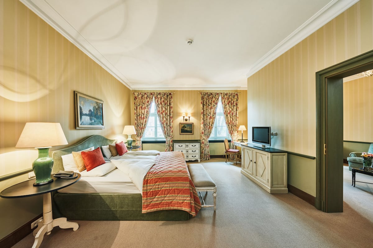 A hotel room with a bed, bedside tables, a desk, a television, and a window with curtains.