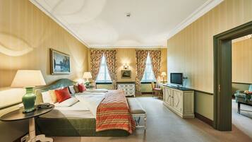 A hotel room with a bed, bedside tables, a desk, a television, and a window with curtains.