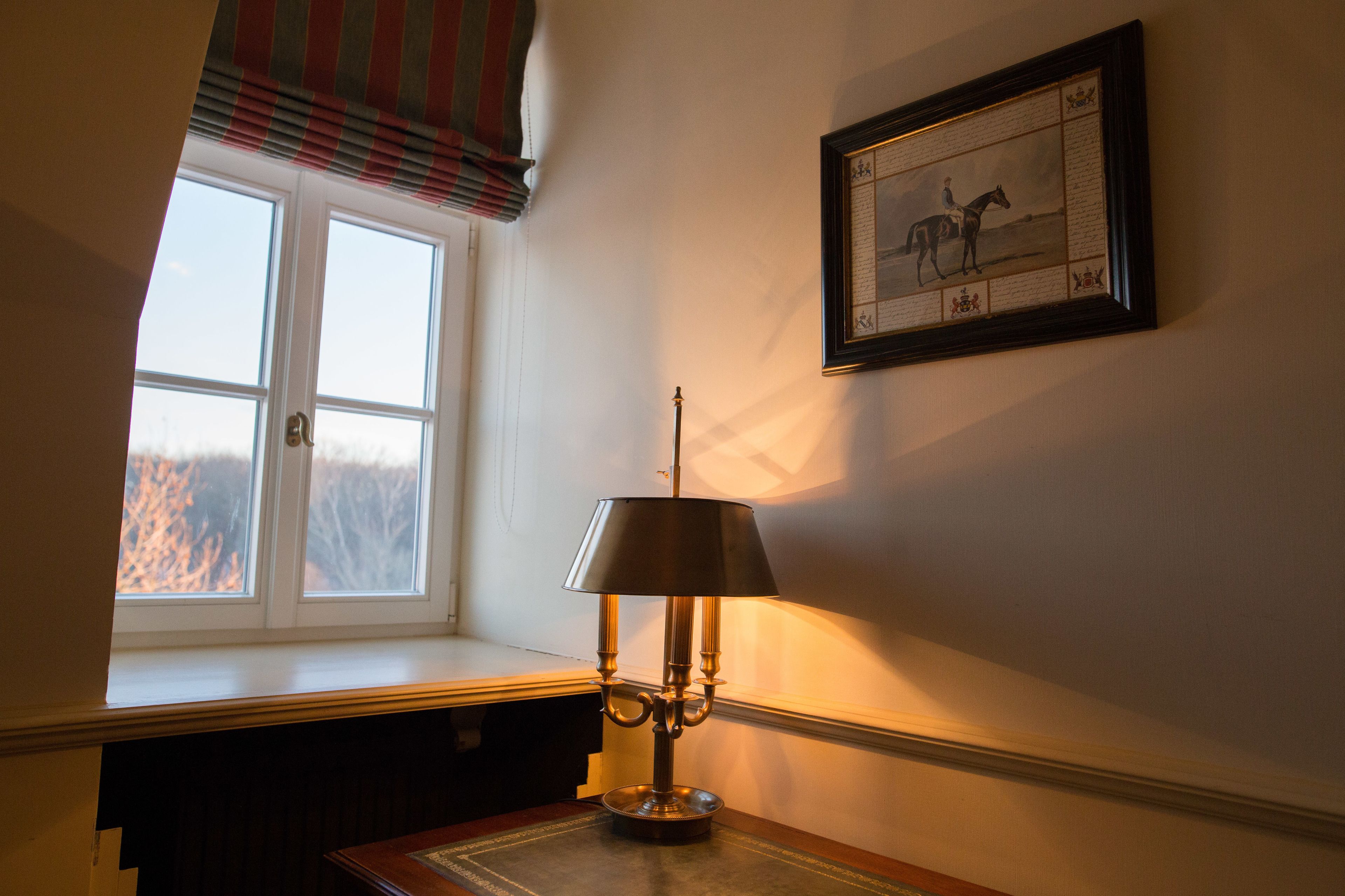 Quarto com janela, luminária de mesa e um quadro na parede.