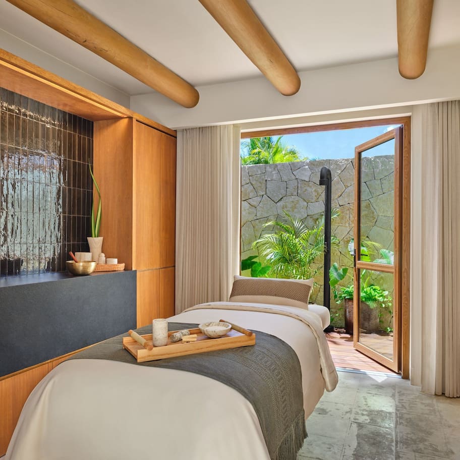 A modern bedroom with a large window, a bathtub, and a wooden shelf with toiletries.