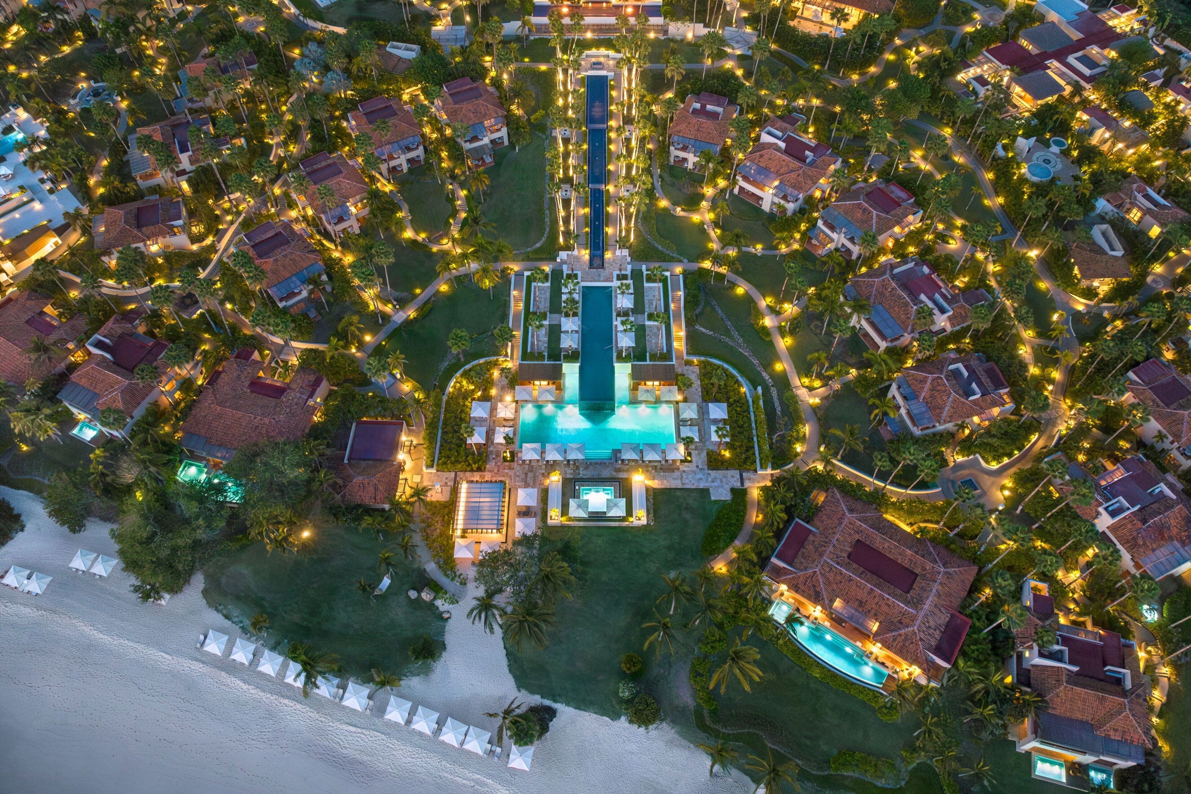 An aerial view of a resort with multiple buildings, a central pool, and a beachfront.