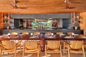 A modern dining area with a long wooden table, matching chairs, and built-in shelves with kitchenware.