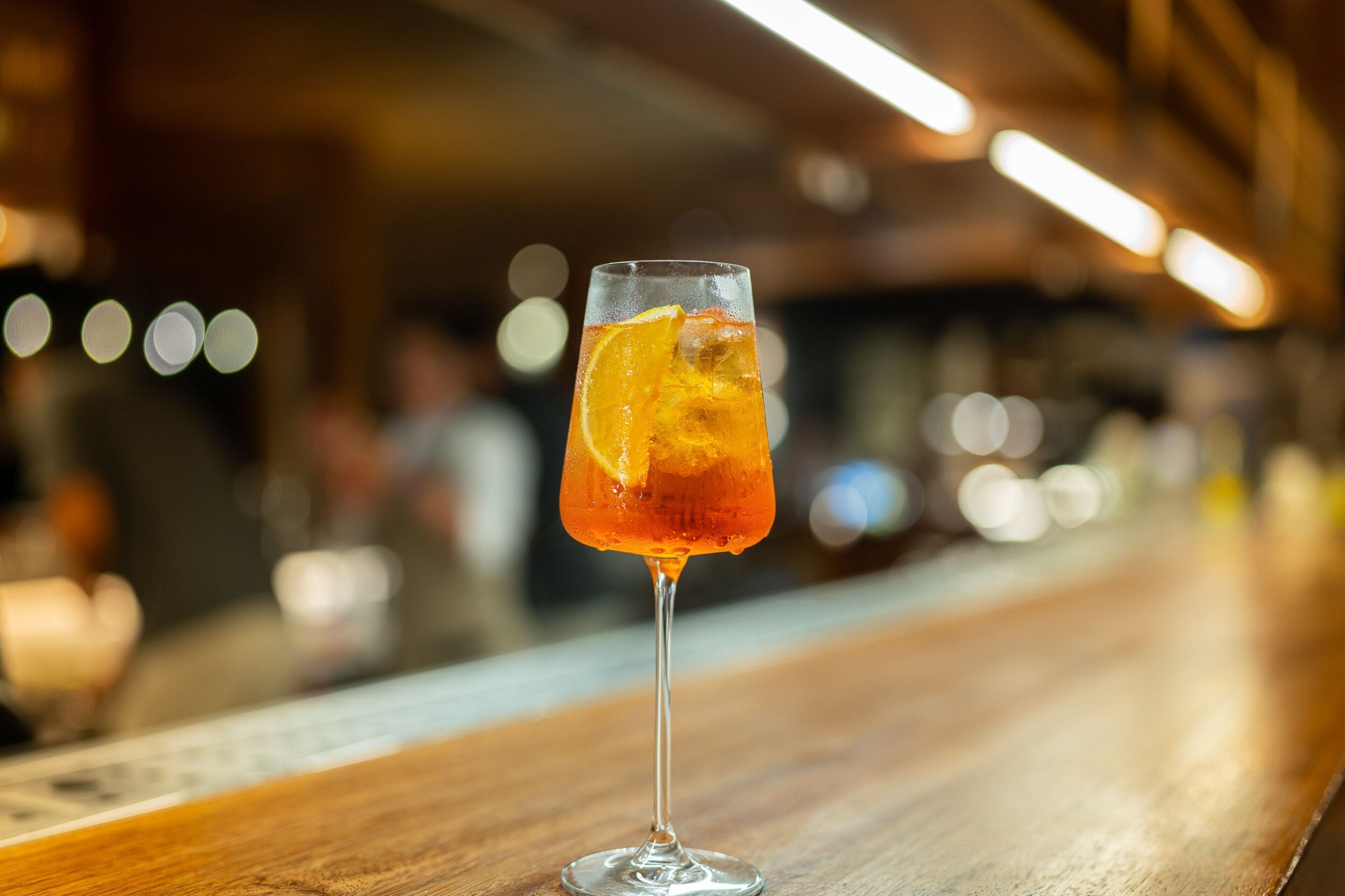 En bardisk med ett glas bärnstensfärgad dryck och en apelsinskiva på en trädisk.